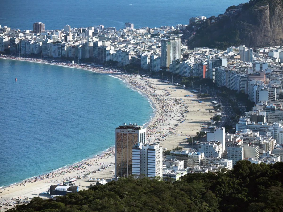 Curva da praia de Copacabana vista do alto, com a faixa de prédios da Avenida Atlântica e o costão ao fundo