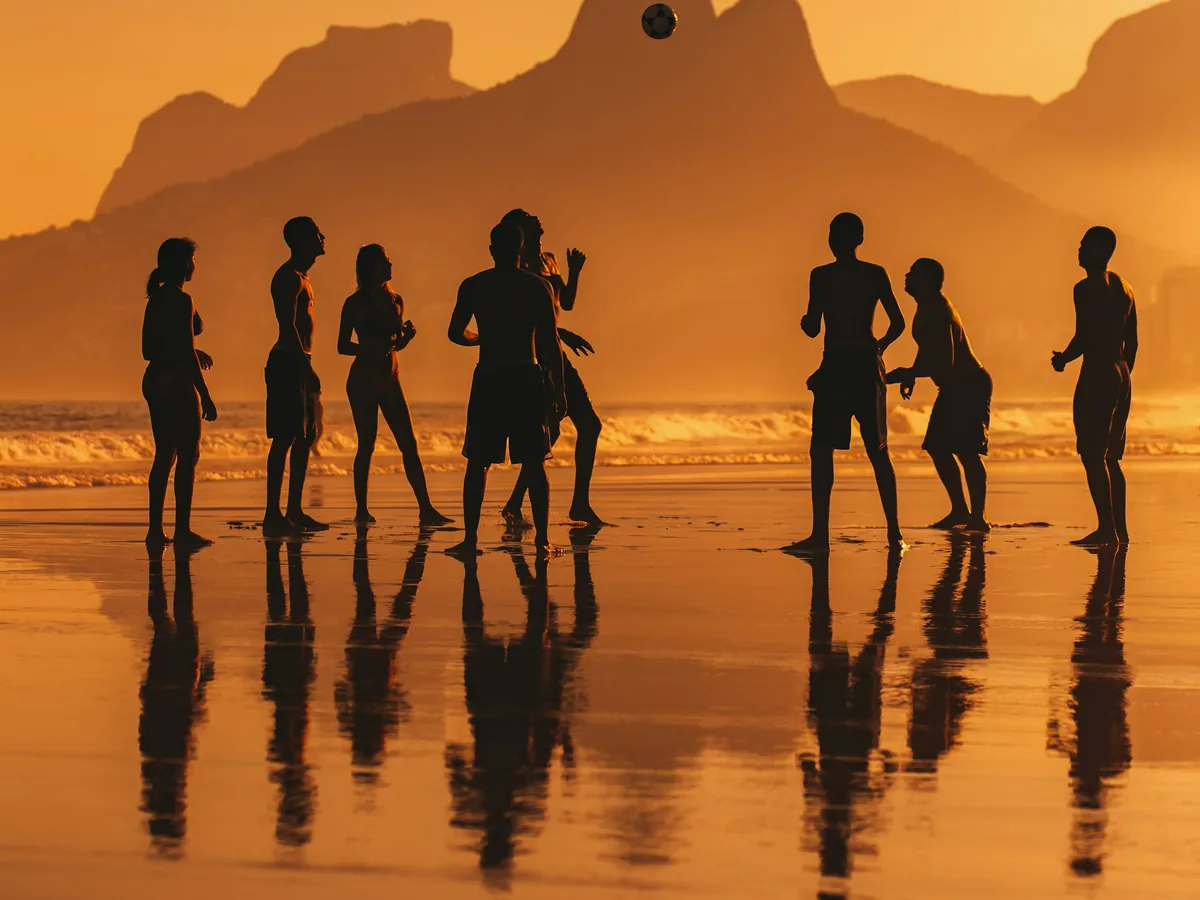 Grupo de pessoas na praia de Ipanema ao pôr do sol, com o Morro Dois Irmãos ao fundo